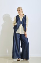 A fashion model stands confidently in a minimalist studio, wearing a denim vest and wide-leg pants
