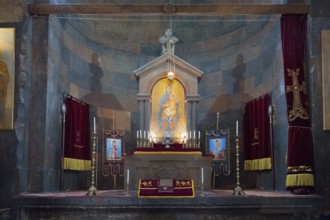 The altar stands in the church with religious icons, candles and deep shades of red, Khor Virap