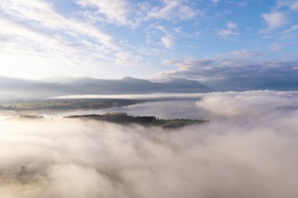 Morning fog hovers over Lake Forggensee with mountains in the background, near Rosshaupten,