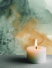 A candle is lit on a table in front of a green and yellow background. The candle's light casts a