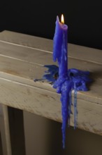 Blue candle lit and melted on a wooden table with a black background