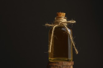 Close-up of a glass bottle with cork stopper and raffia rope with rosemary oil on a dark background