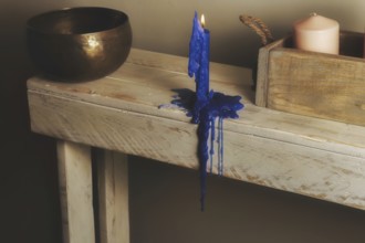 Lighted and melted blue candle, Tibetan bowl and a wooden tray with candles on a wooden table