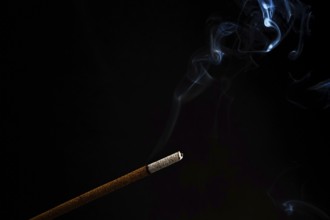 Close-up of a burning incense with white smoke coming out illuminated on a black background