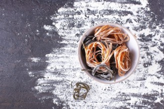 Pasta with carrots and spinach in a round plate on a floured table, space for text