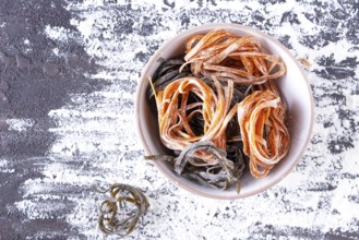 Pasta with carrots and spinach in a round plate on a table covered with flour, top view, space for