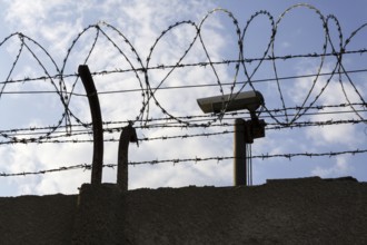 Security camera behind barbed wire fence stretched around prison walls Prague Czech republic