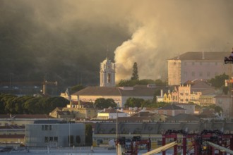 Lisbon church tower in sundown light surrounded by historic buildings and column of rising smoke in