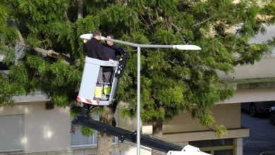 Two unrecognizable utility workers operate hydraulic lift to repair street light in residential