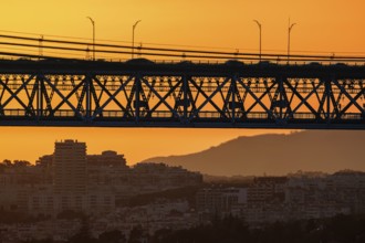 Striking close-up of famous 25 de Abril bridge, its silhouette against bright orange sunset sky.