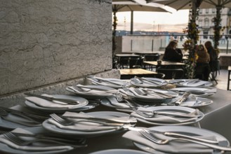 Plates neatly arranged with forks, knives, and napkins on stone countertop at outdoor restaurant in
