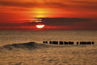 A vivid sunset over the sea with gentle waves and an orange sky creating a tranquil atmosphere.