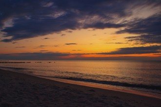 A tranquil beach sunset with vibrant colors in the sky and gentle waves lapping at the sandy shore.