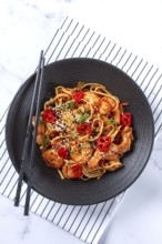 Delicious shrimp stir-fry with noodles and colorful vegetables served in a black bowl on a striped