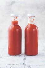 Two clear glass bottles hold vibrant red sauce, likely a spicy or tangy condiment, in a well-lit