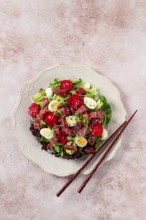 Salad with fresh tuna, cherry tomatoes and quail eggs and avacado, served with chopsticks