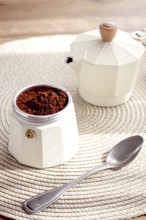 Geyser coffee maker with ground coffee and a spoon on the background of a woven rug, coffee