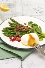 Poached egg with fork, asparagus, bacon slices and herbs, on a white plate, breakfast, close-up, no