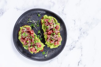 Fresh tuna tartare on avocado spread toast with microgreens served on a black plate