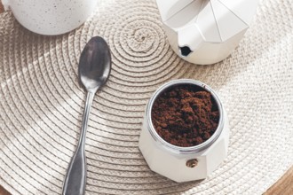 Geyser coffee maker with ground coffee and a spoon on the background of a woven rug, coffee