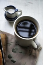 A cup of black coffee with a small pot of milk