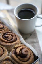 Freshly baked cinnamon rolls on a wooden board with a cup of coffee