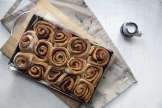Freshly baked cinnamon rolls on a wooden board with a small pot of milk