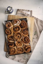 Freshly baked cinnamon rolls on a wooden board with a small pot of milk