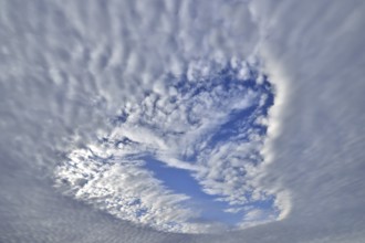 Heart-shaped hole in low-lying closed cloud cover provides a view of the blue sky with sheep