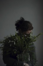 Woman holding ostrich with grasses, face covered