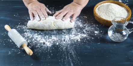 Baker's hands carefully kneading uncooked dough on a dark kitchen counter, preparing traditional
