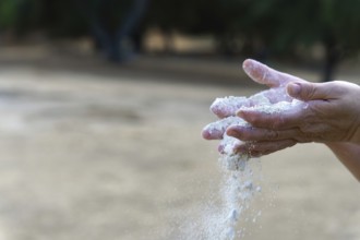 Hands releasing loose sand, grains falling through aged fingers to symbolize time, fragility,
