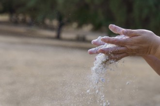 Hands pouring white sand, symbolizing the passage of time, impermanence, and the fleeting moments