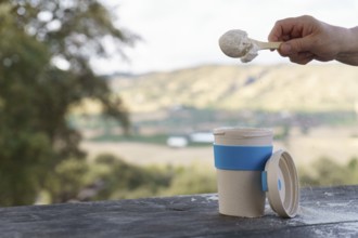 Hand scooping protein powder into a reusable cup on a wooden table, preparing a healthy lifestyle