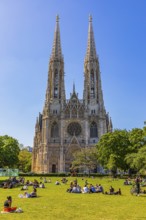 Young people enjoy the spring sun on the meadow in front of the neo-gothic votive church, Vienna,