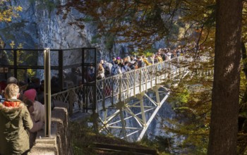 People queue on Marienbrücke near Neuschwanstein Castle, in an autumn forest landscape, Schwangau,