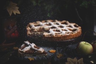 Icing sugar falls on apple pie surrounded by autumn leaves in a dark environment