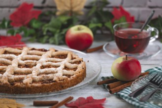 Apple cake with powdered sugar next to tea and apples, surrounded by autumn leaves and cinnamon