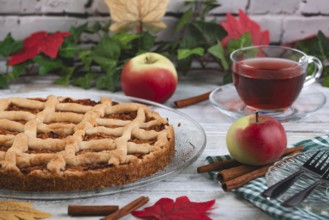 Apple pie with tea and apples surrounded by autumn leaves and cinnamon sticks