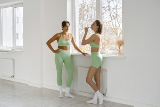 Two women in green activewear take a break during their fitness stretching class. They are standing