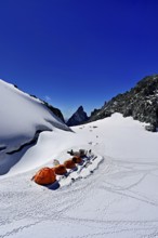 Tents on snowy areas, in the background the l'Aiguille Noire de Peuterey mountain, Pointe