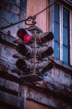 An old, weathered traffic light hangs in front of a building façade, shows red