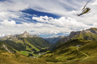 A helicopter flies over a mountainous landscape with blue skies and clouds