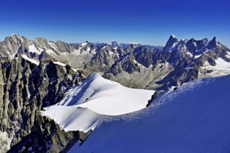 Mountaineers climb over a snow-covered ridge with Grandes Jorasses mountain in the background,