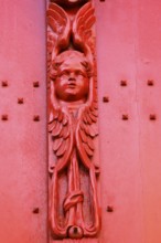 Red wooden door with decorative carving of an angel figure at the entrance to the historic St.
