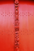 Red wooden door with decorative carvings and an angel figure at the entrance to the historic St.