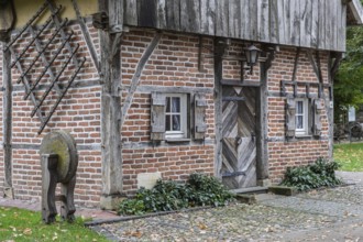 Small half-timbered house with wooden door, whetstone and cobblestones, framed by ivy and leaves,