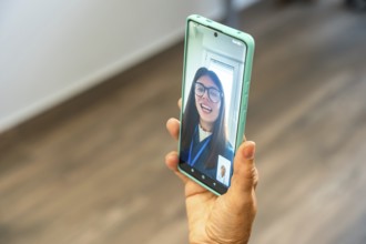 Person holding a smartphone, engaging in a virtual medical consultation with a doctor appearing on