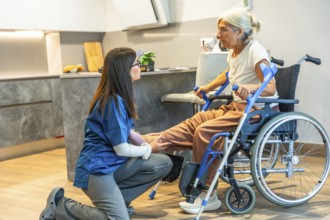 Nurse assisting an elderly woman in a wheelchair with home physiotherapy, providing gentle physical