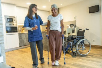 Young female nurse helping a happy elderly woman recovering from injury, walking with crutches